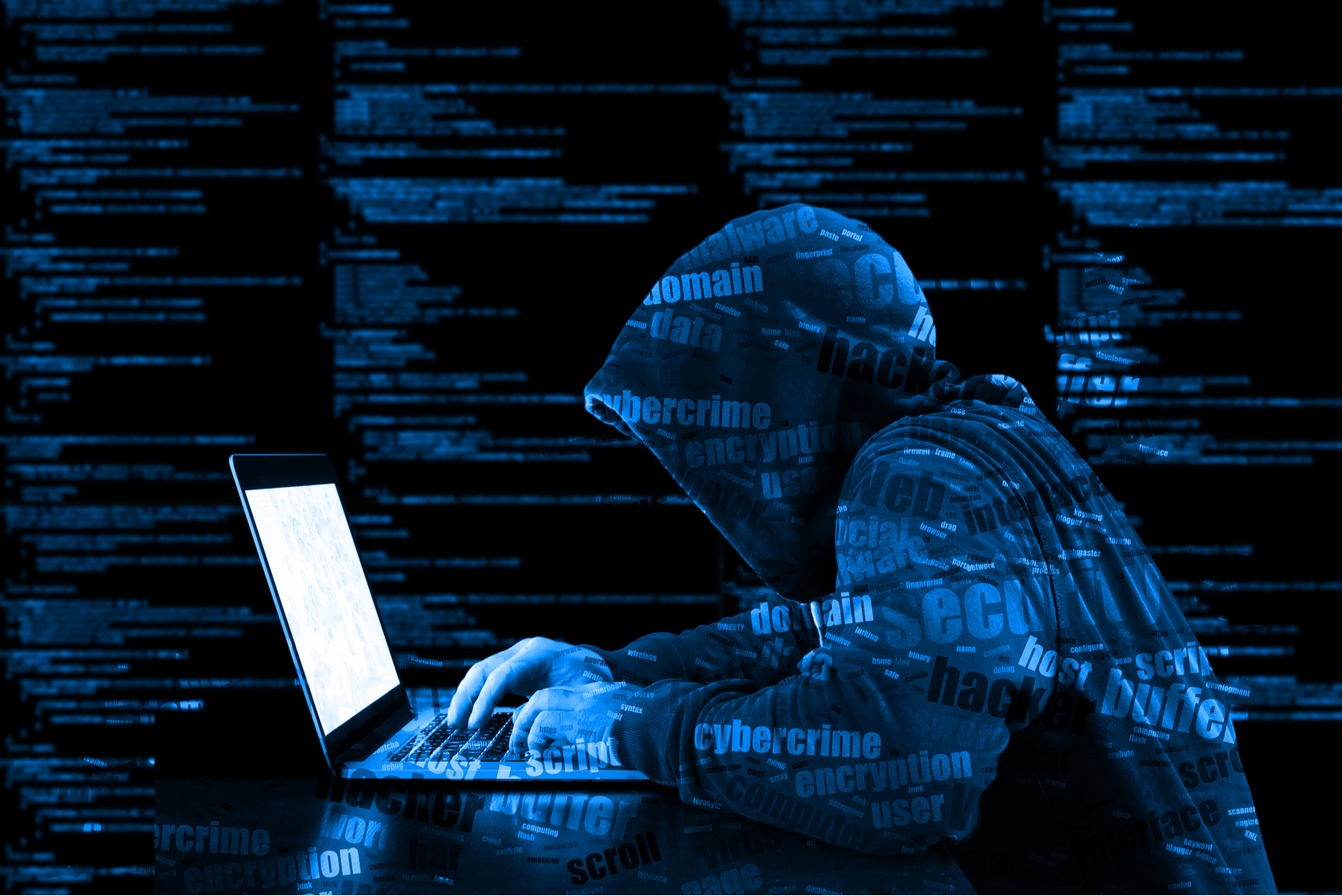 Hooded cyber criminal performing a data breach on laptop