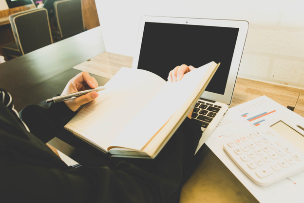 person with open notebook in front of a laptop