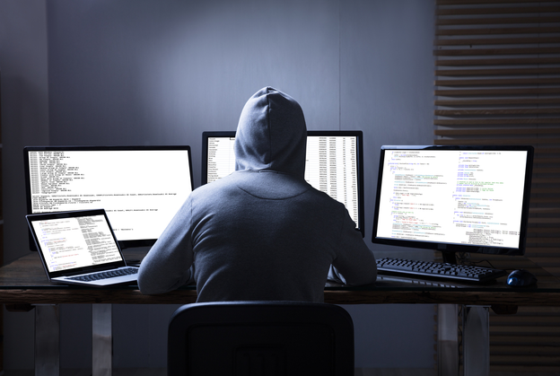 Hooded hacker in front of computer screens