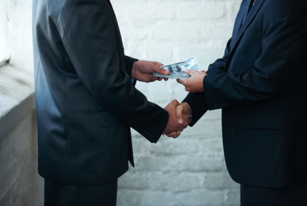 two men in suits shaking hands and making a deal over money