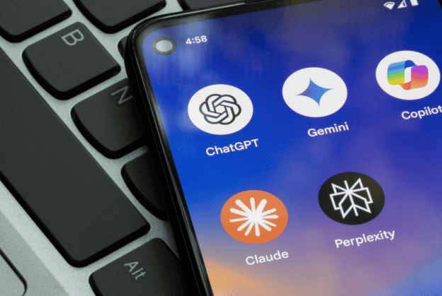 Smartphone screen displaying five AI chatbot app icons—ChatGPT, Gemini, Copilot, Claude, and Perplexity, resting on a laptop keyboard.